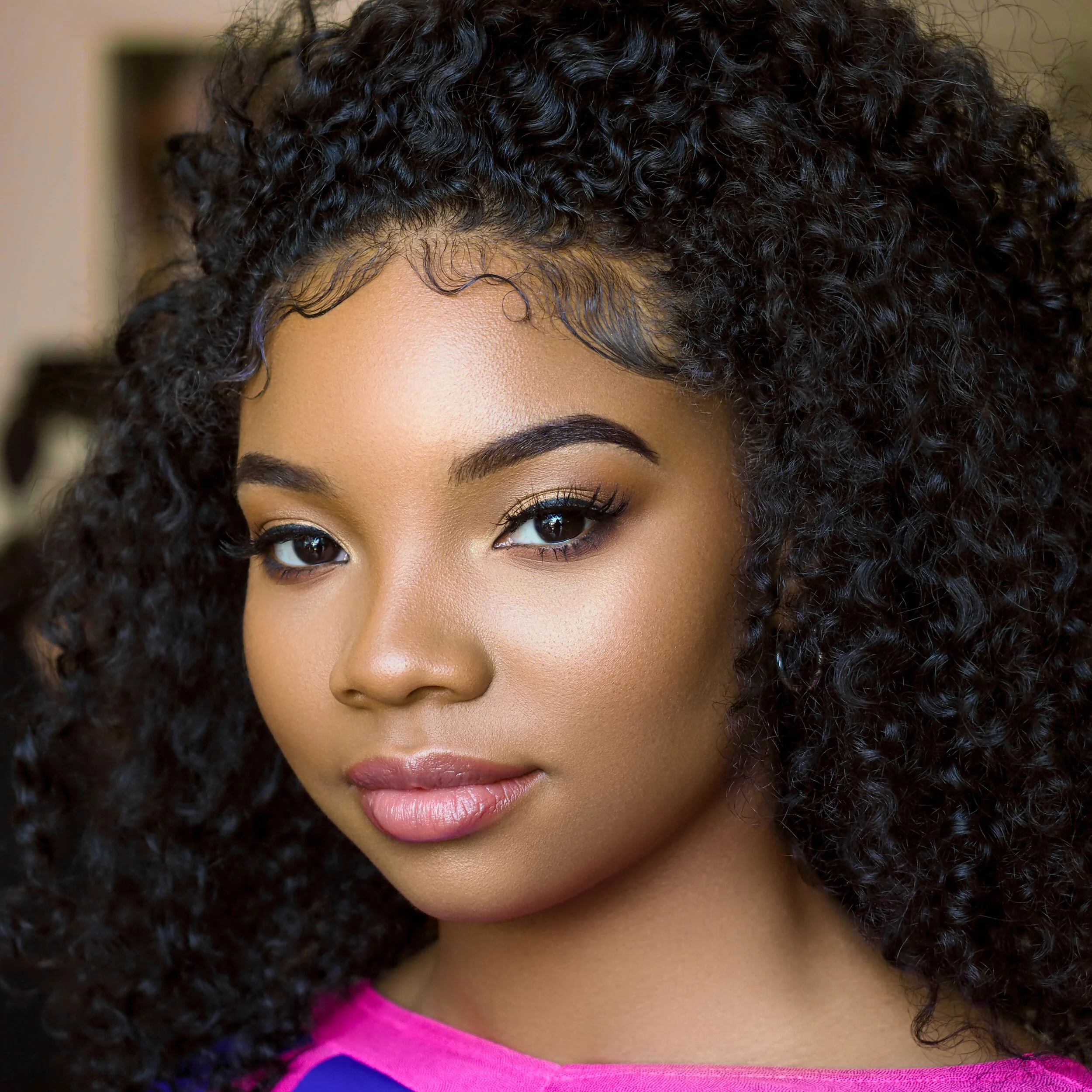 A young woman with curly dark hair, light makeup, and a bright pink and purple top.