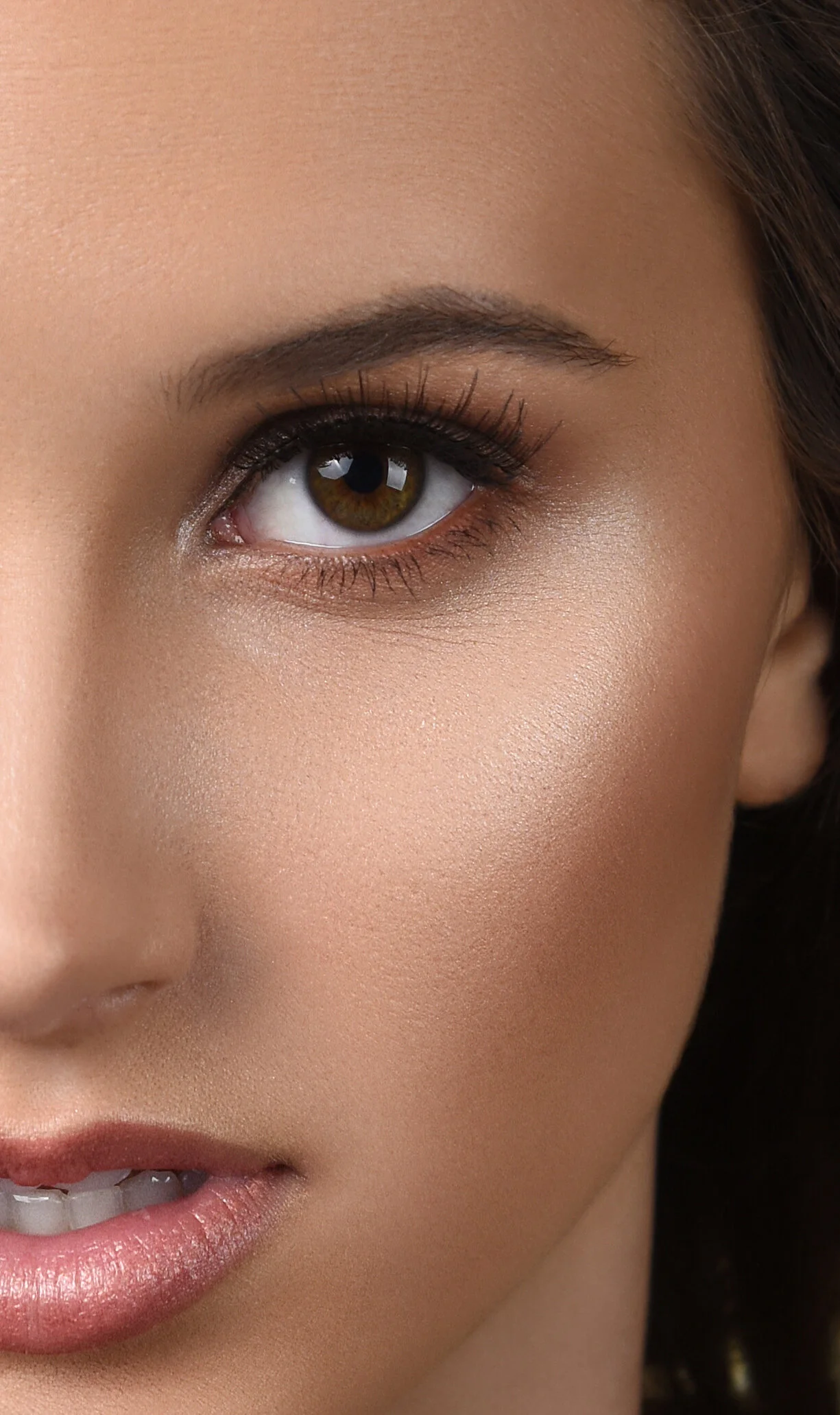 Close-up of a woman's face highlighting her eye, eyebrow, and part of her nose and lips with makeup and smooth skin.