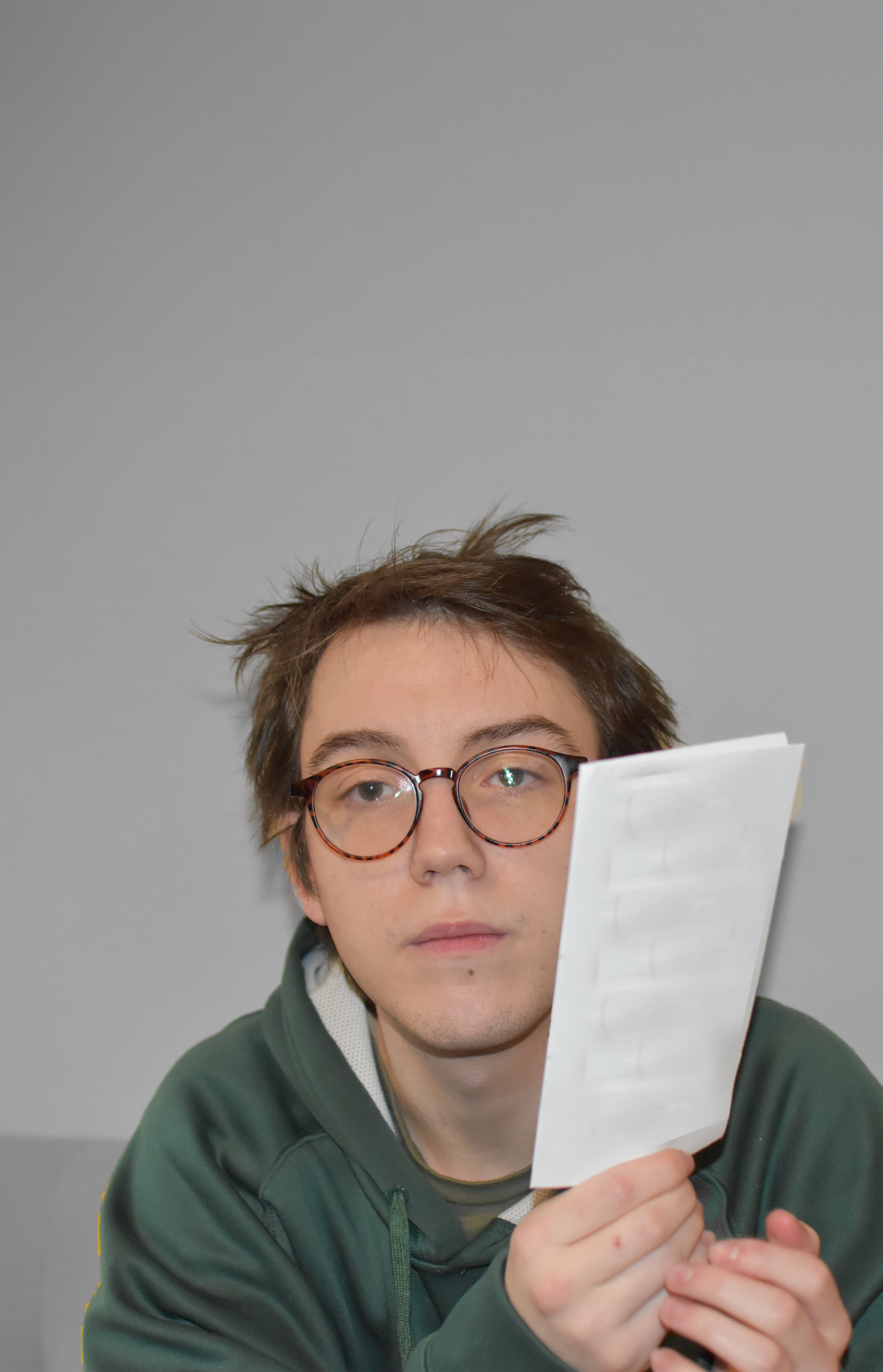 Person wearing glasses and a green hoodie holding a white card.