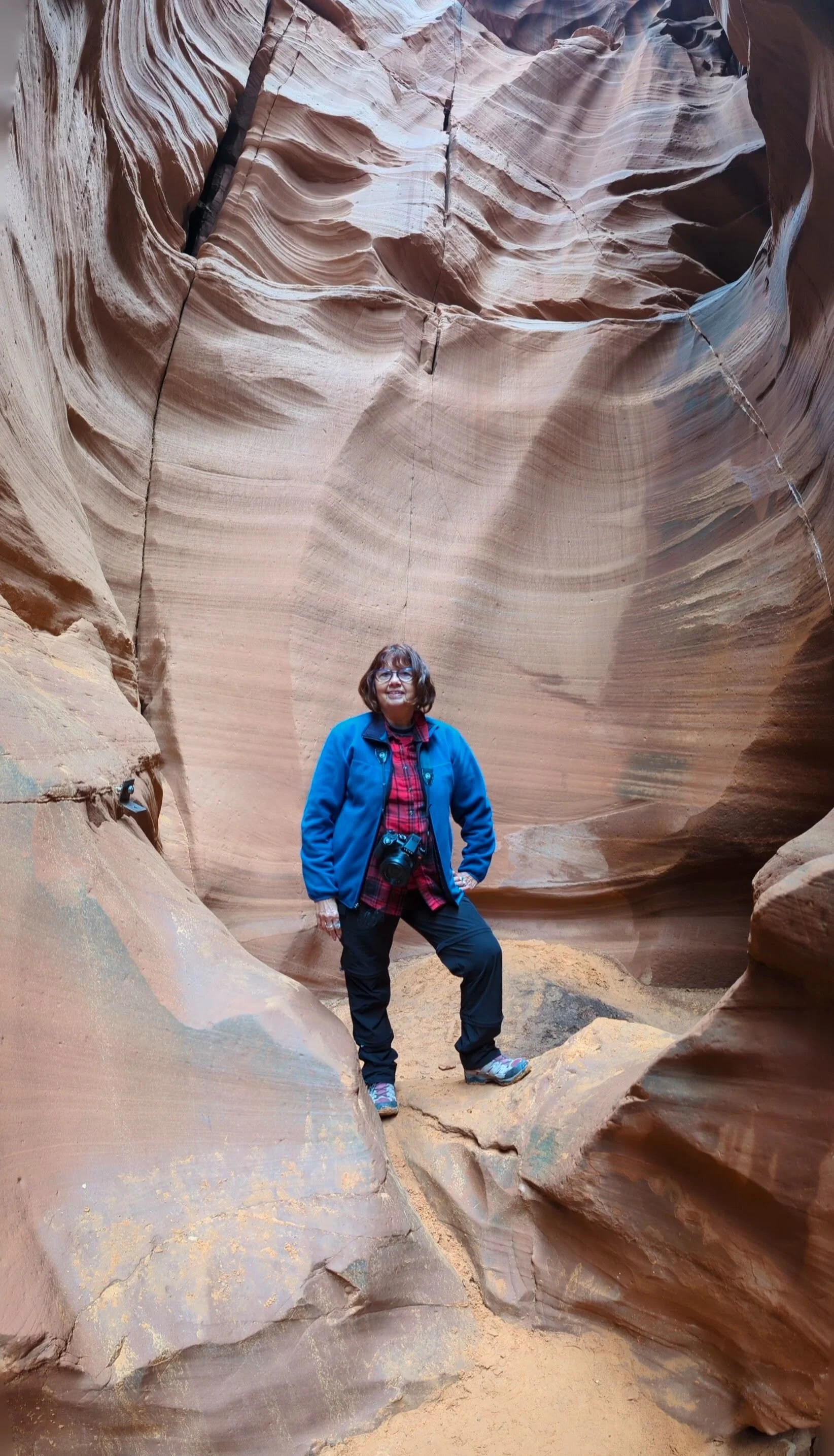 Roxanne standing inside a slot canyon with towering, layered reddish-brown rock walls.
