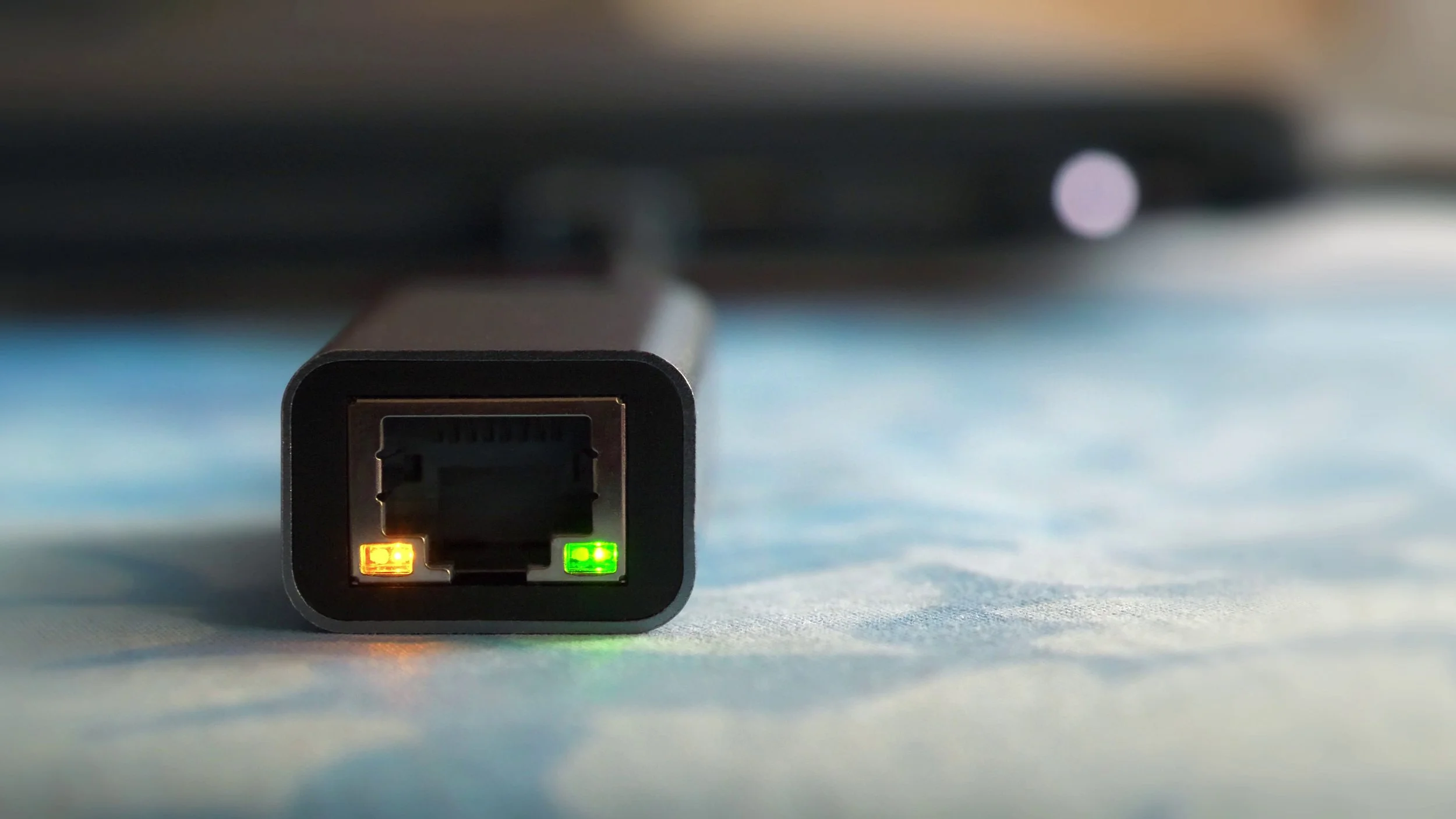 Close-up of an Ethernet network cable connector with LED lights, resting on a surface with a blurred background.