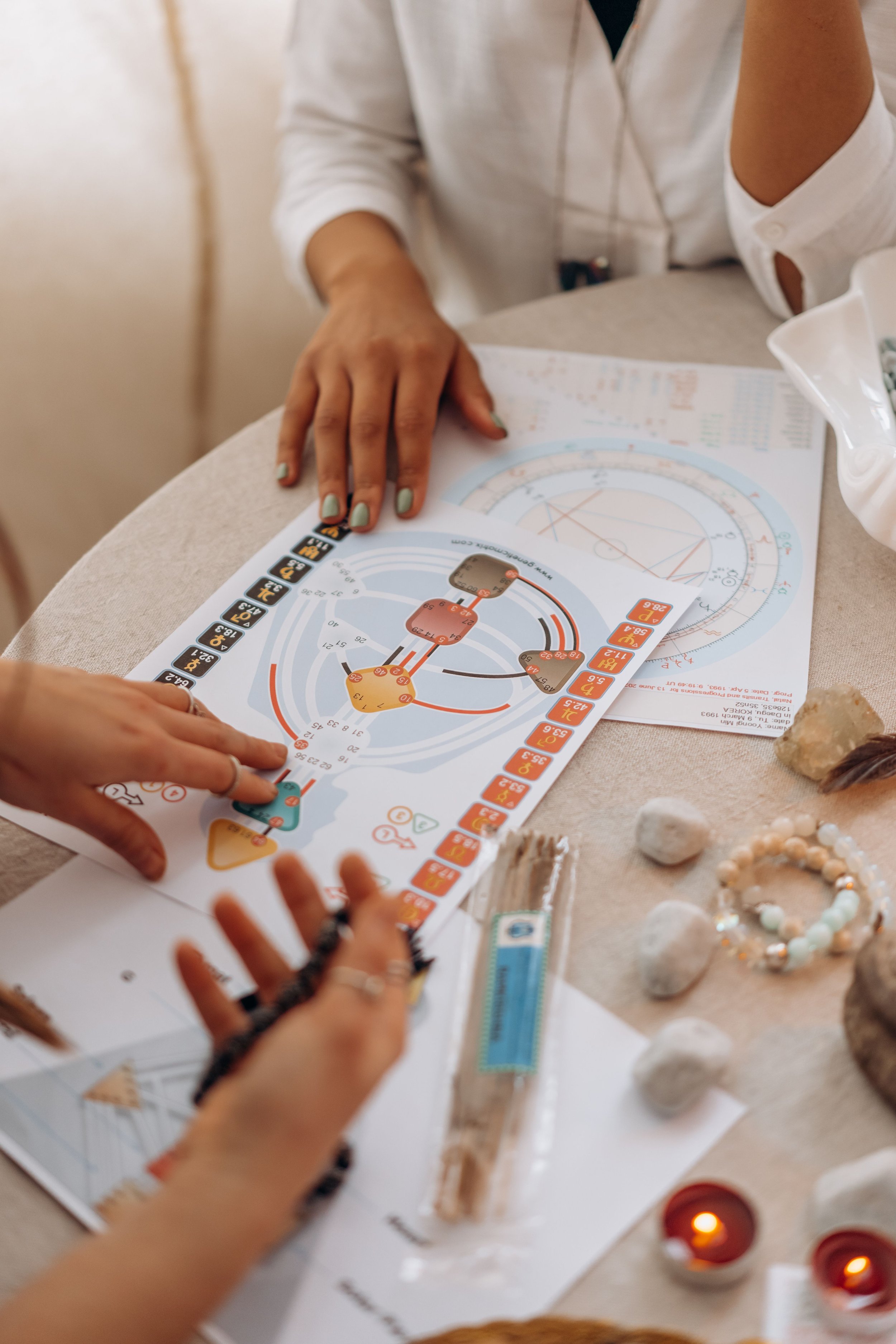 A serene scene of astrology and human design chart reading with crystals, candles, and hands in focus.