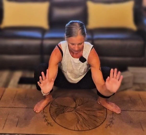 Woman in a yoga pose on a wooden table in a living room, with a black couch and yellow pillows in the background.