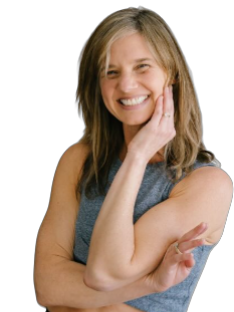 A woman with shoulder-length blonde hair smiling, wearing a sleeveless gray top, touching her face and arm against a black background.