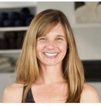 A woman with long, straight, light brown hair smiling in an indoor setting.