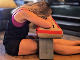 A woman sitting on the floor with her head resting on a striped bag placed on a concrete block, appearing to be upset or exhausted.