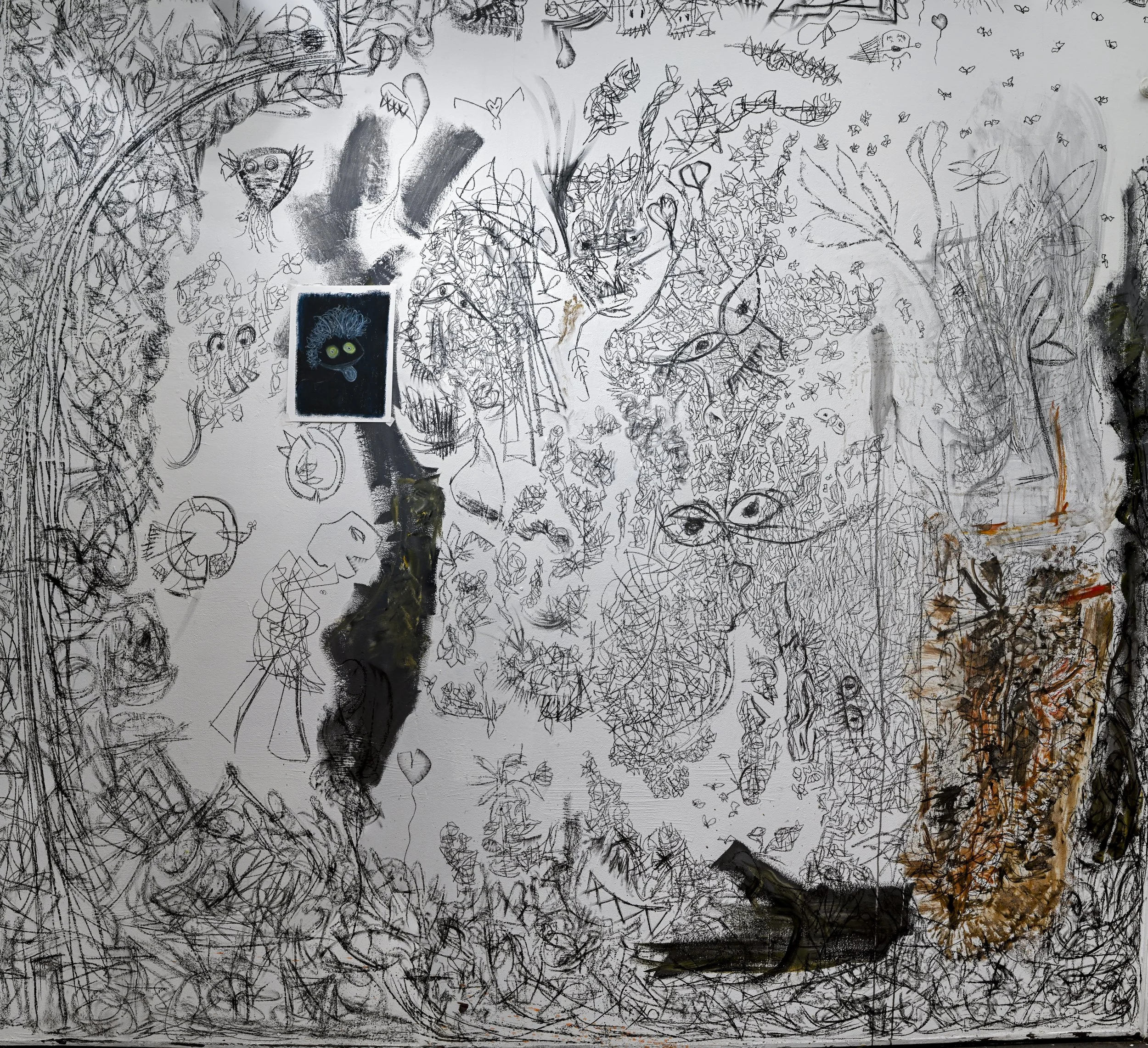 A wall covered with black ink sketches of various abstract and semi-figurative characters, faces, animals, and creatures, with some colored and photographic elements, including a prominent blue and green face in the center.