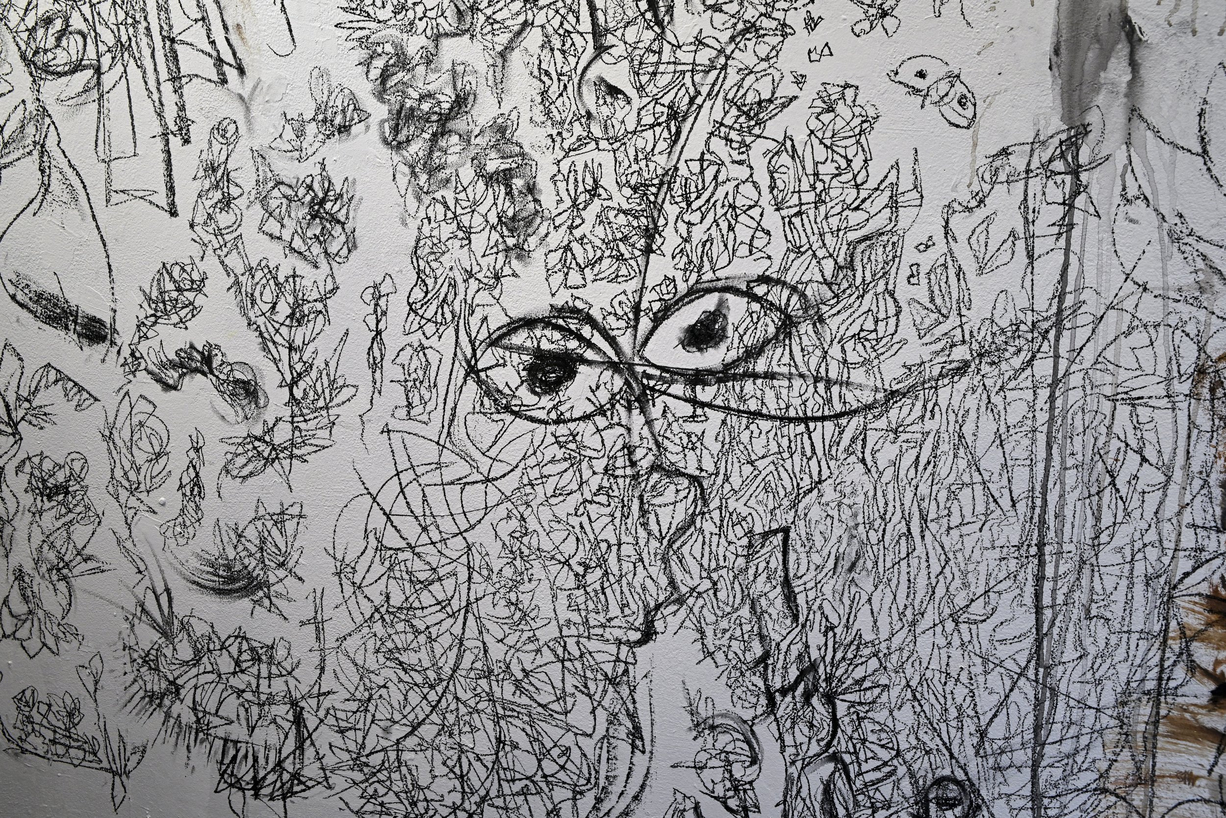 A black and white abstract drawing of a face with large, expressive eyes, surrounded by chaotic, scribbled lines and patterns.