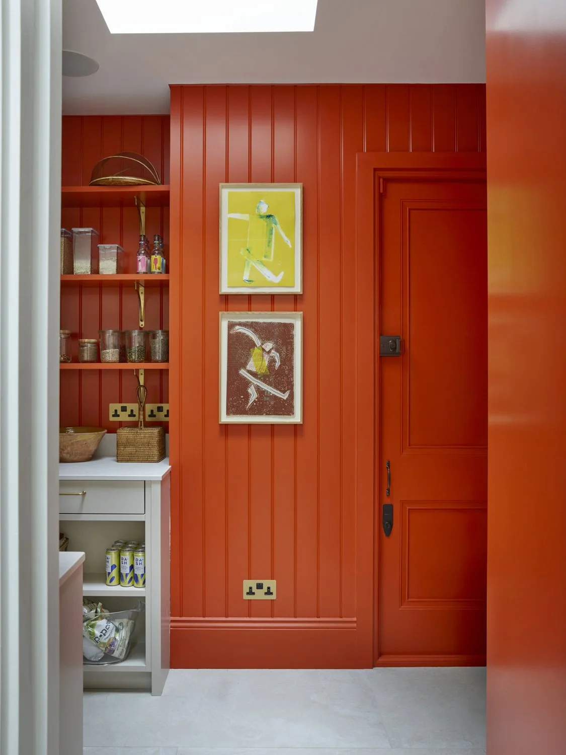A blue desk with gold knobs, a green-shaded brass lamp, and a cordless phone. To the left, a tall blue bookshelf with empty shelves. On the wall above the desk, a framed sketch of a building and trees.