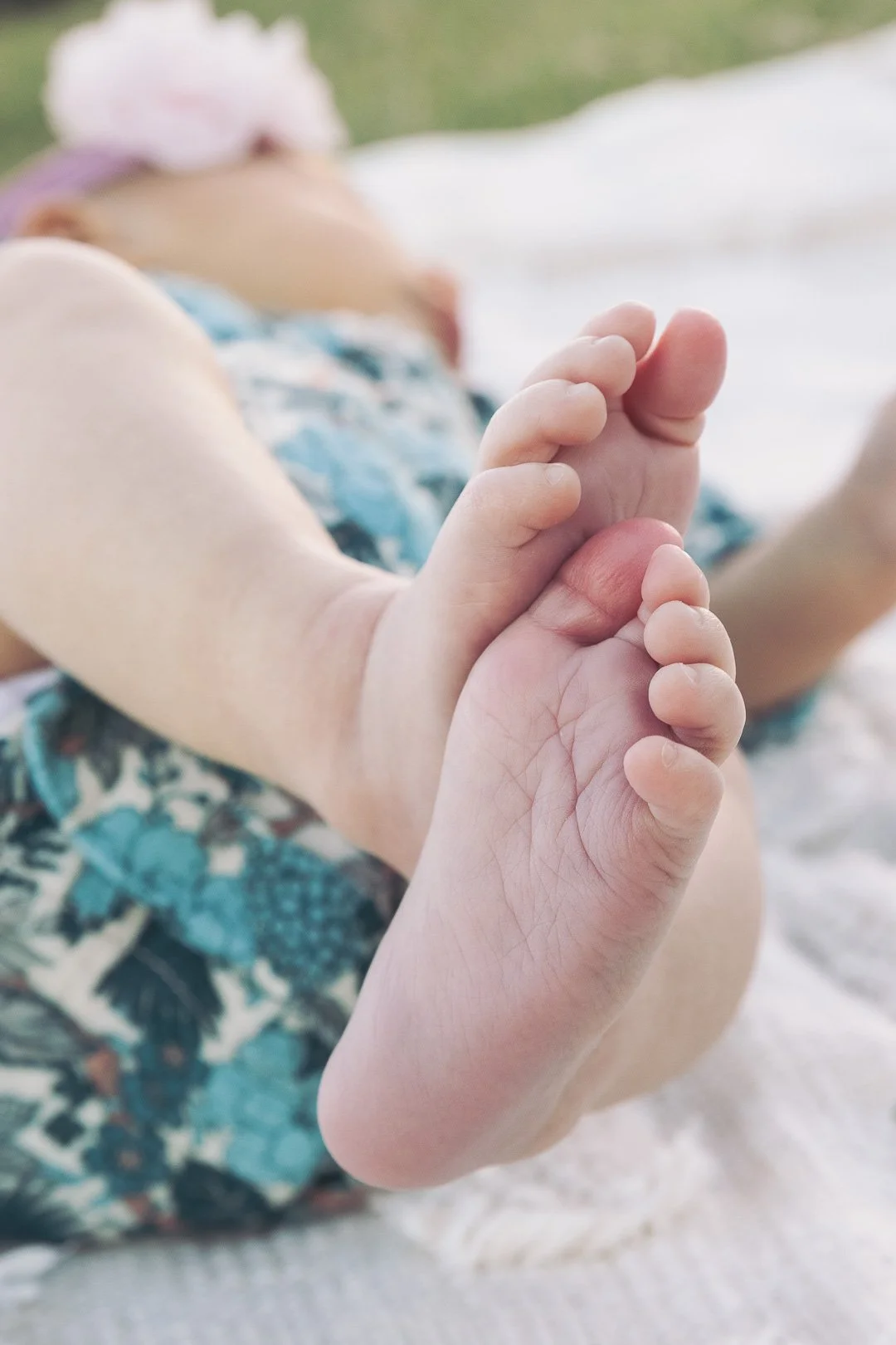 Close-up of a baby's feet with a background of a blurred infant lying on a blanket outdoors.
