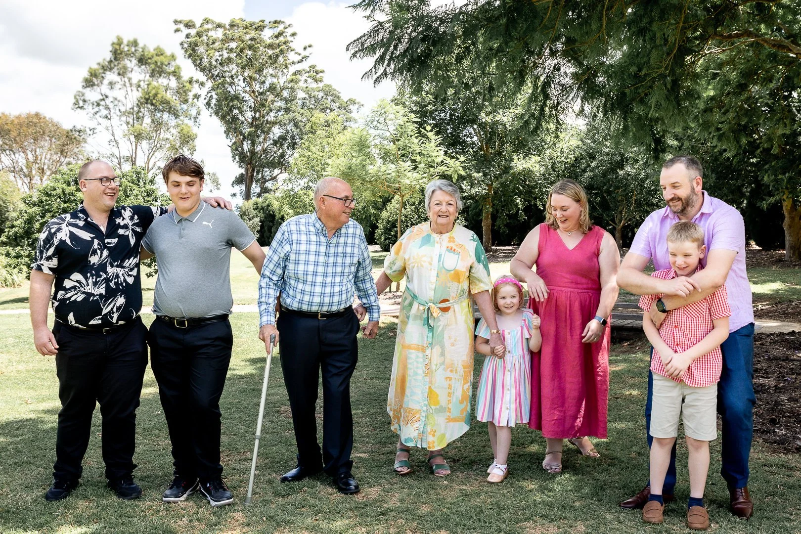 Family group walking together outdoors in a park, smiling and enjoying a sunny day.