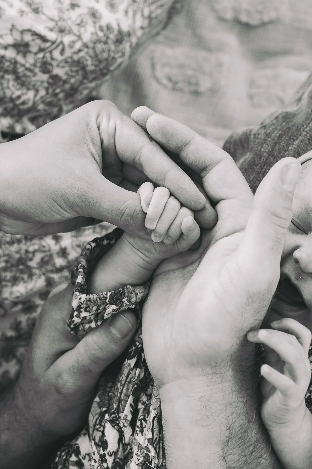 Multiple hands, a mixture of adults and children, holding and touching each other in a gesture of care and connection, with one small child's hand being held by adult hands.