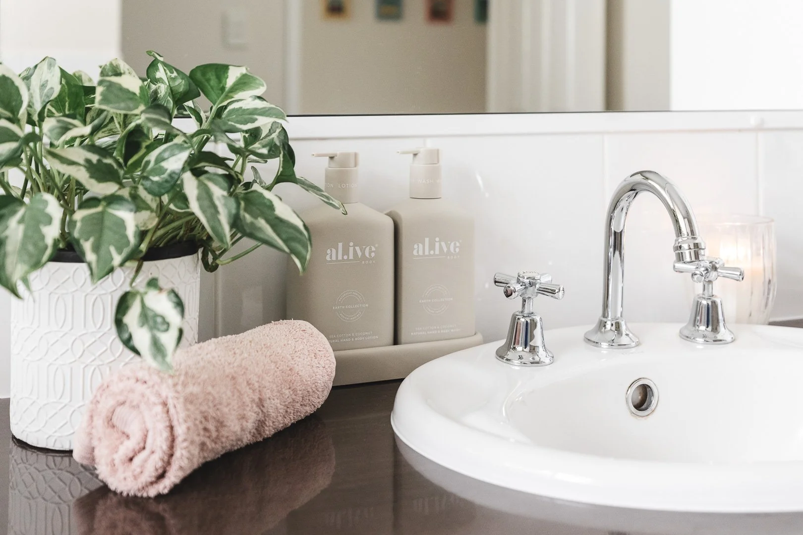 Bathroom sink with a towel, potted plant, and lotion bottles nearby.