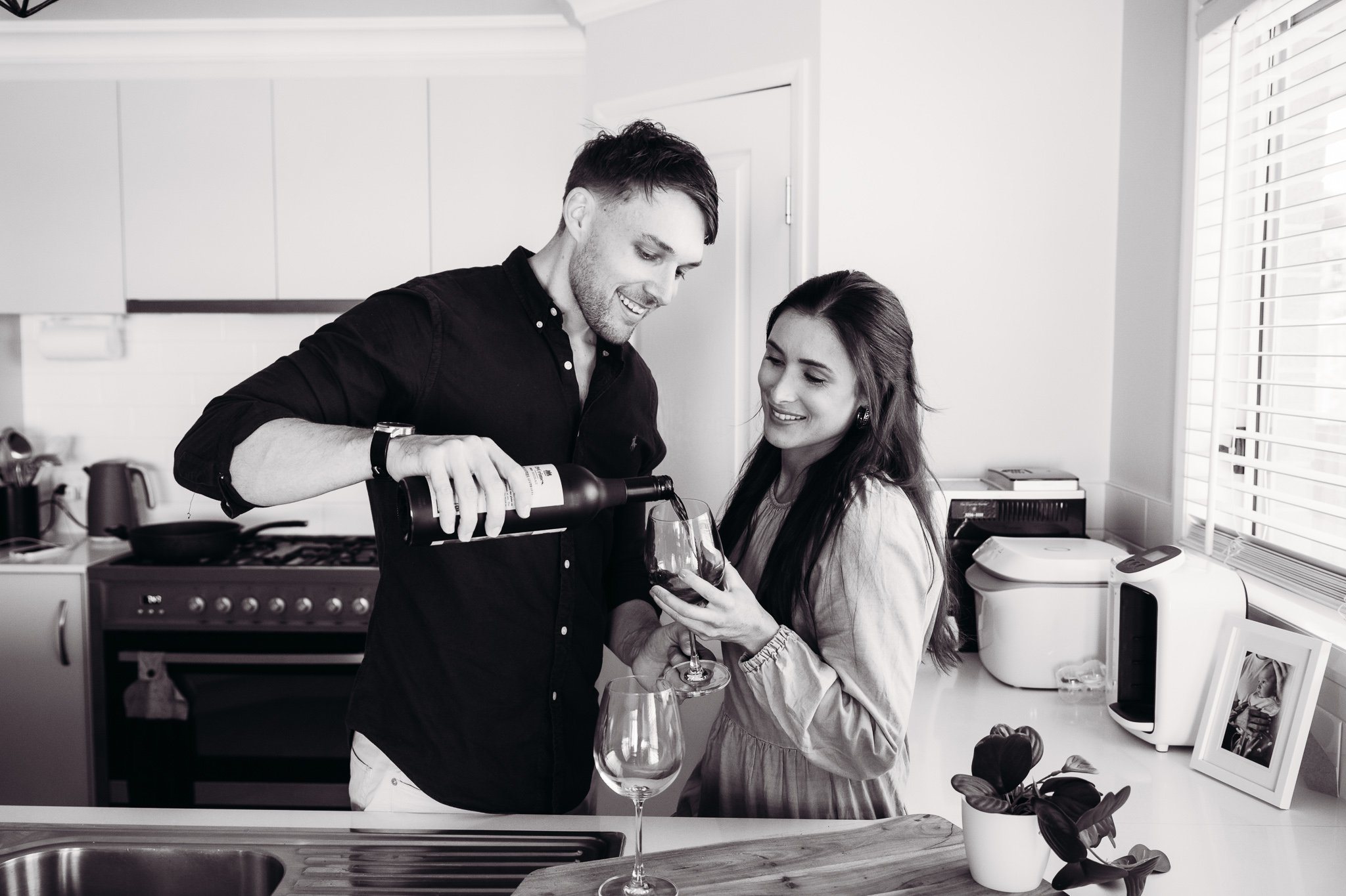 A man and woman pouring red wine into glasses in a modern kitchen.