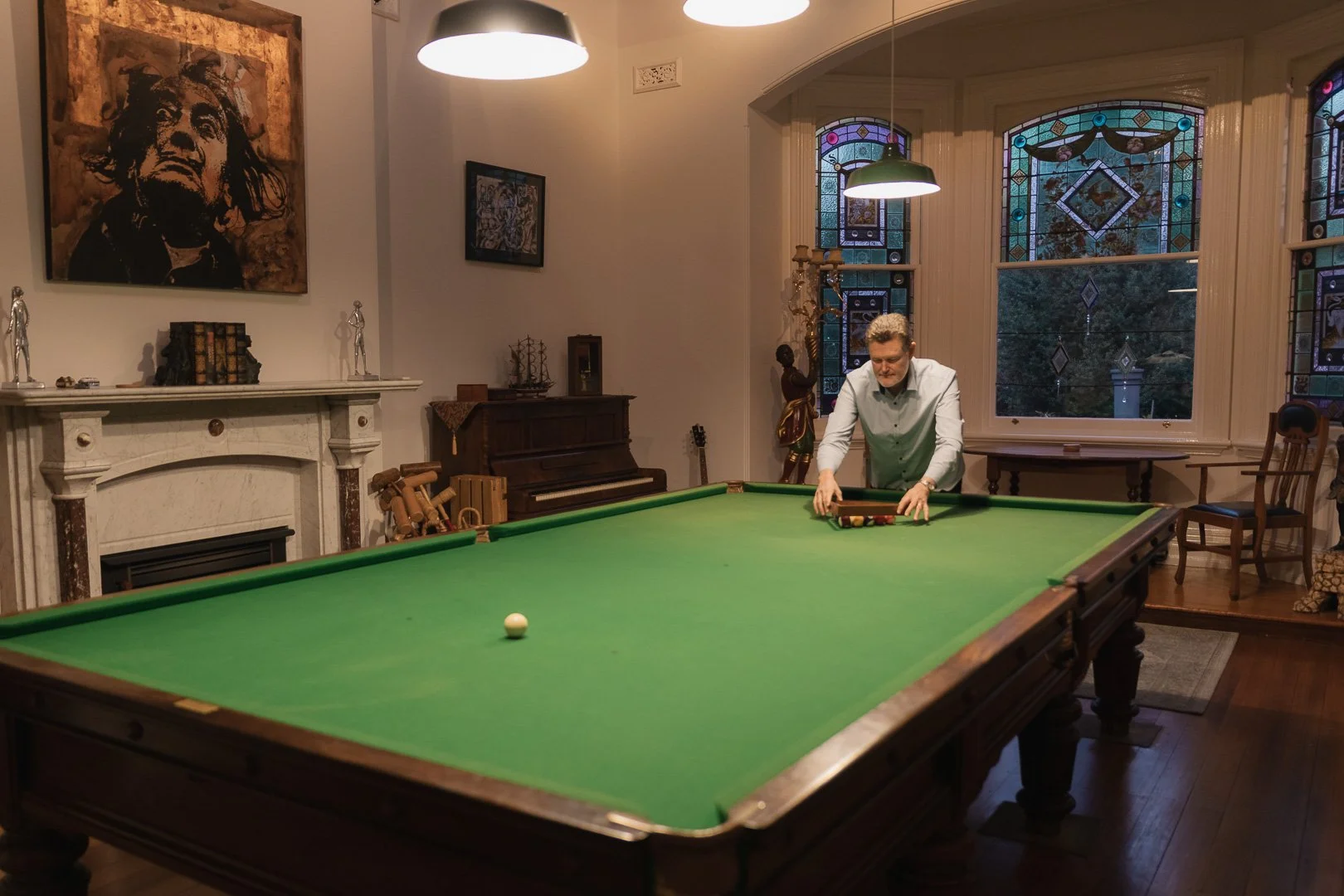 A man is setting up a shot next to a pool table in a living room with stained glass windows, artwork, and various decorative items. Accommodation photography in Toowoomba - Laurene Bardsly Photography.