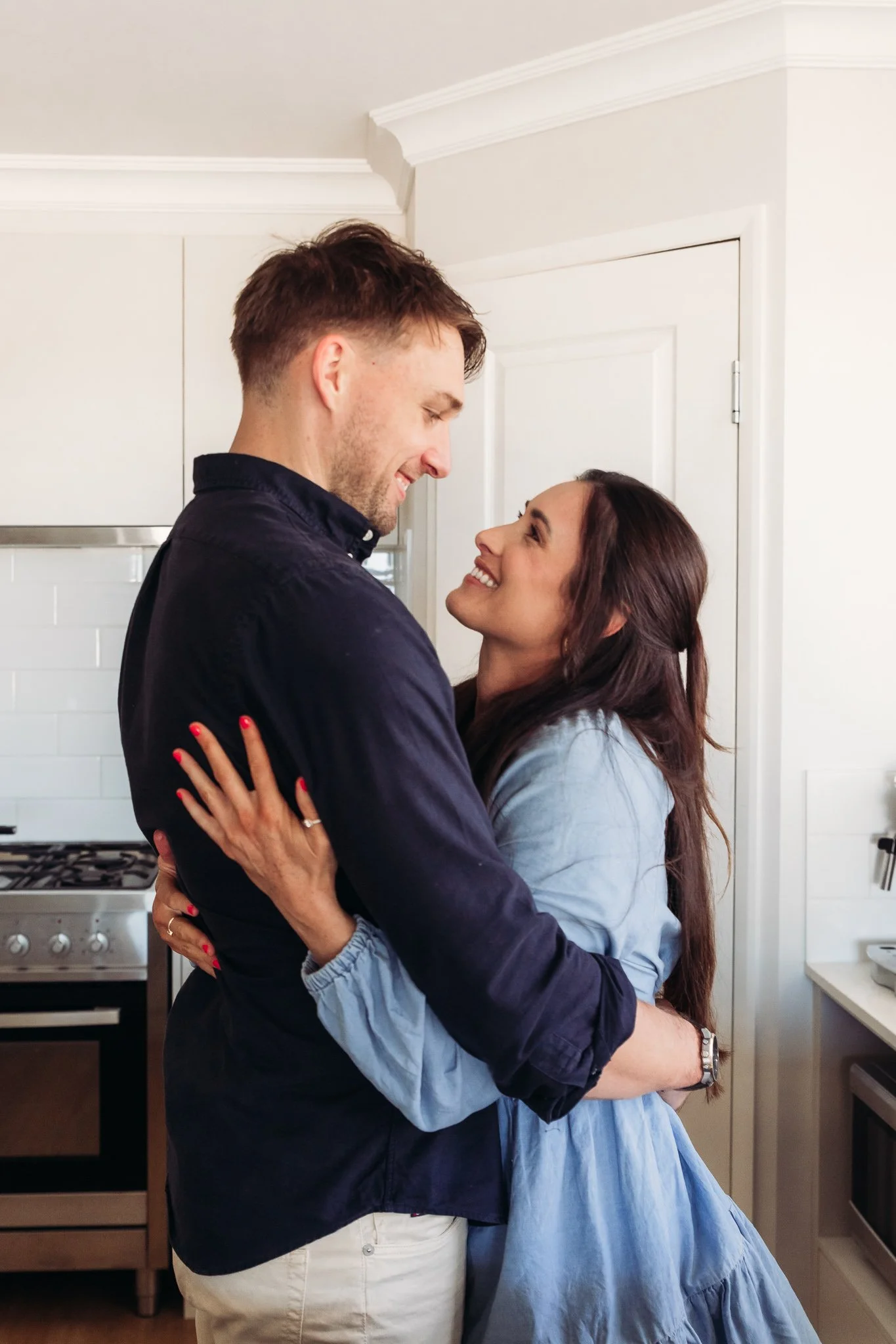 A couple sharing an affectionate embrace and smiling at each other in a kitchen.