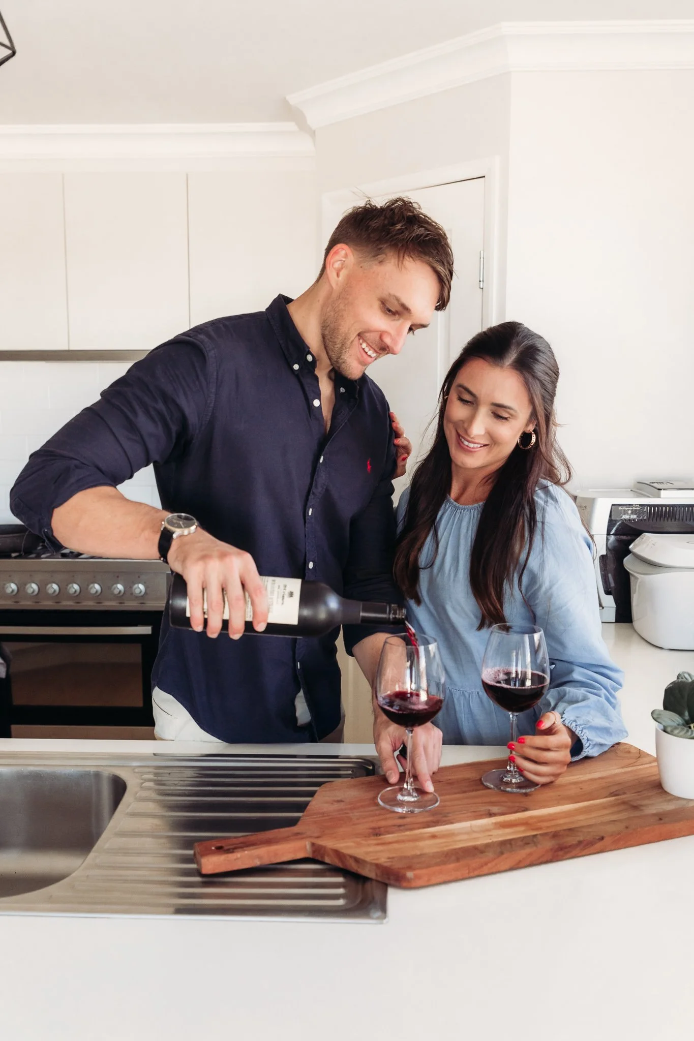 A couple enjoying wine in a modern kitchen; the man is pouring wine into glasses held by the woman at the kitchen counter.