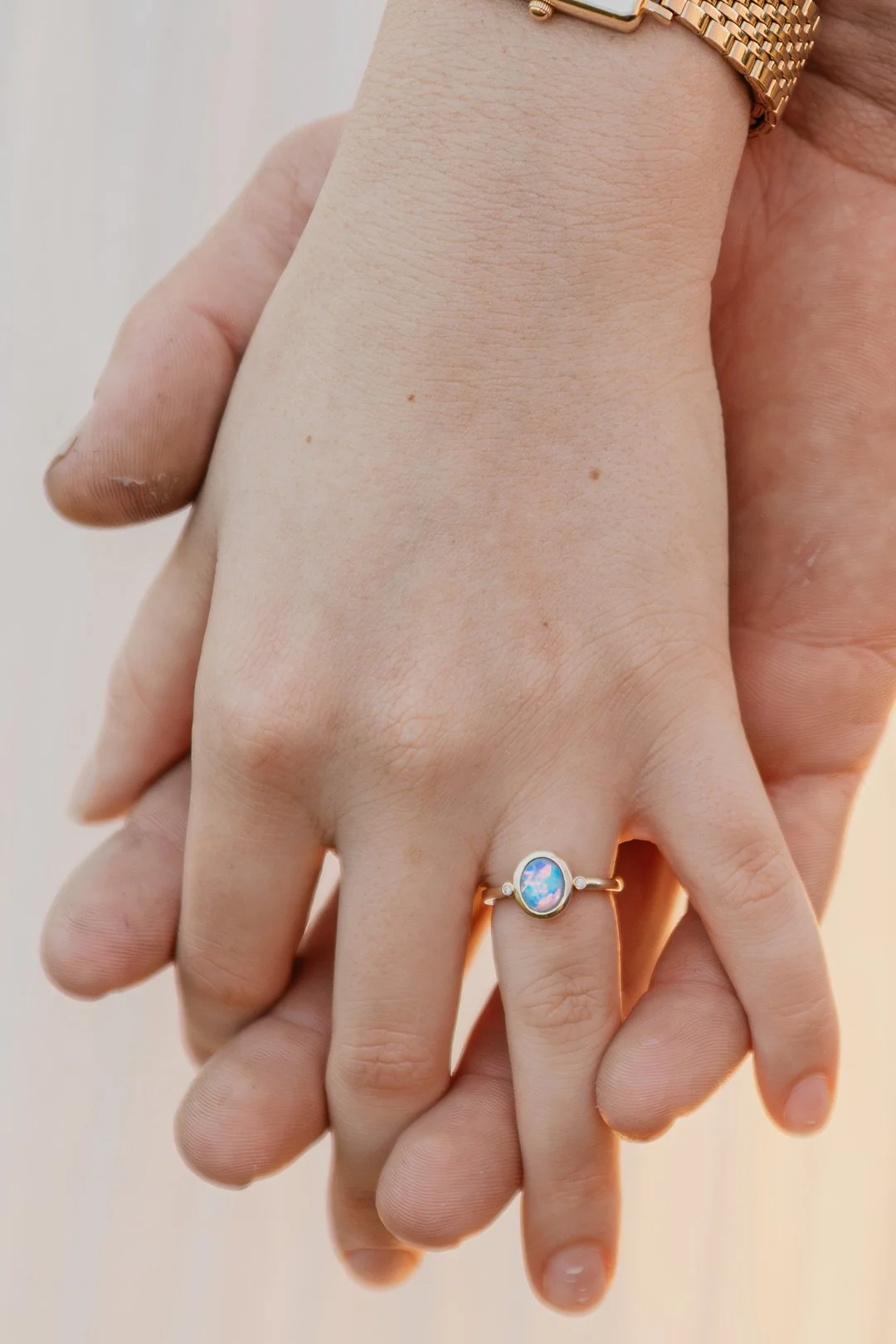 Close-up of a hand with a gold ring featuring a round opal gemstone on the index finger, and a gold bracelet on the wrist.