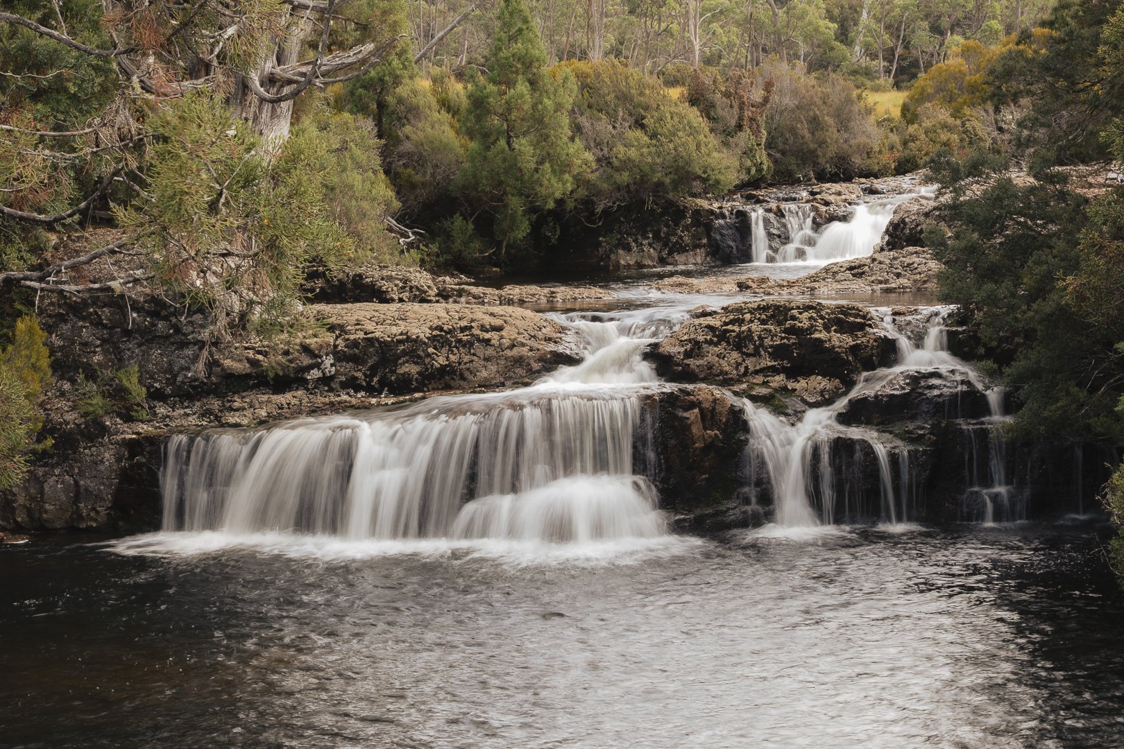 A multi-tiered waterfall flowing over rocks in a wooded landscape with trees and bushes. Landscape photographer in Toowoomba.
