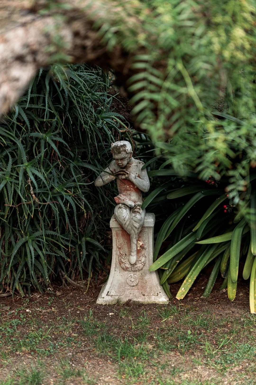 A small statue of a boy sitting on a pedestal, surrounded by green foliage.