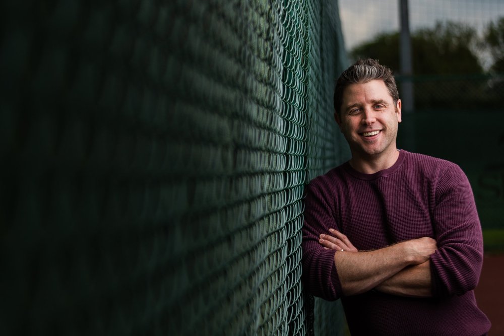 A confident man leaning against a wall with his arms crossed