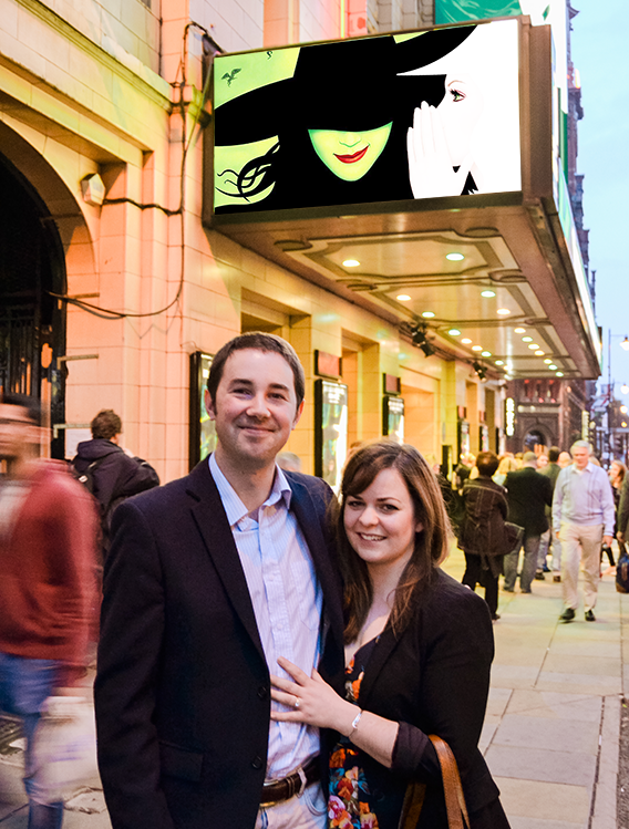A smiling man and woman standing on a busy city sidewalk at dusk.