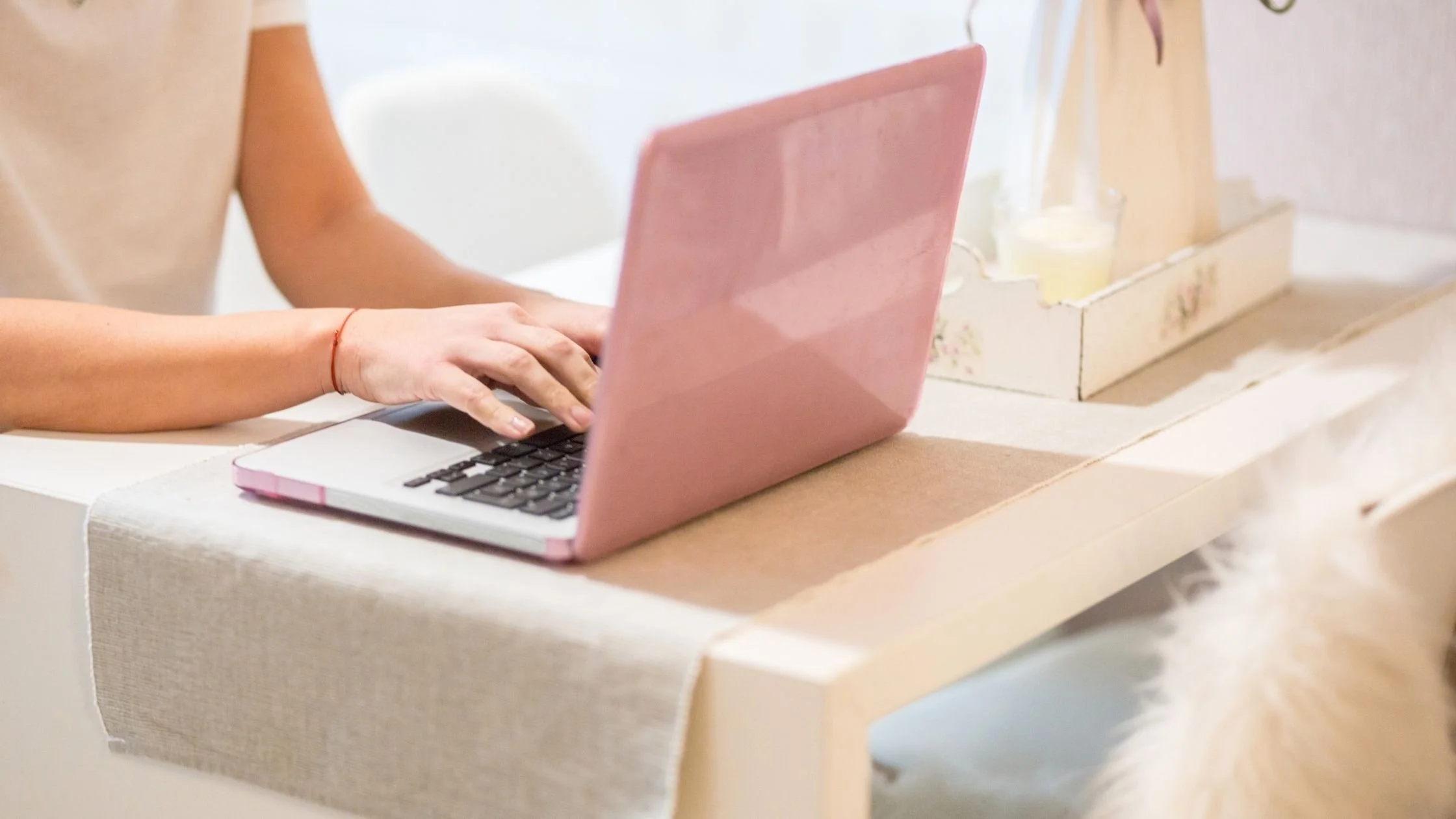 person using pink laptop on a minimalist white wooden desk