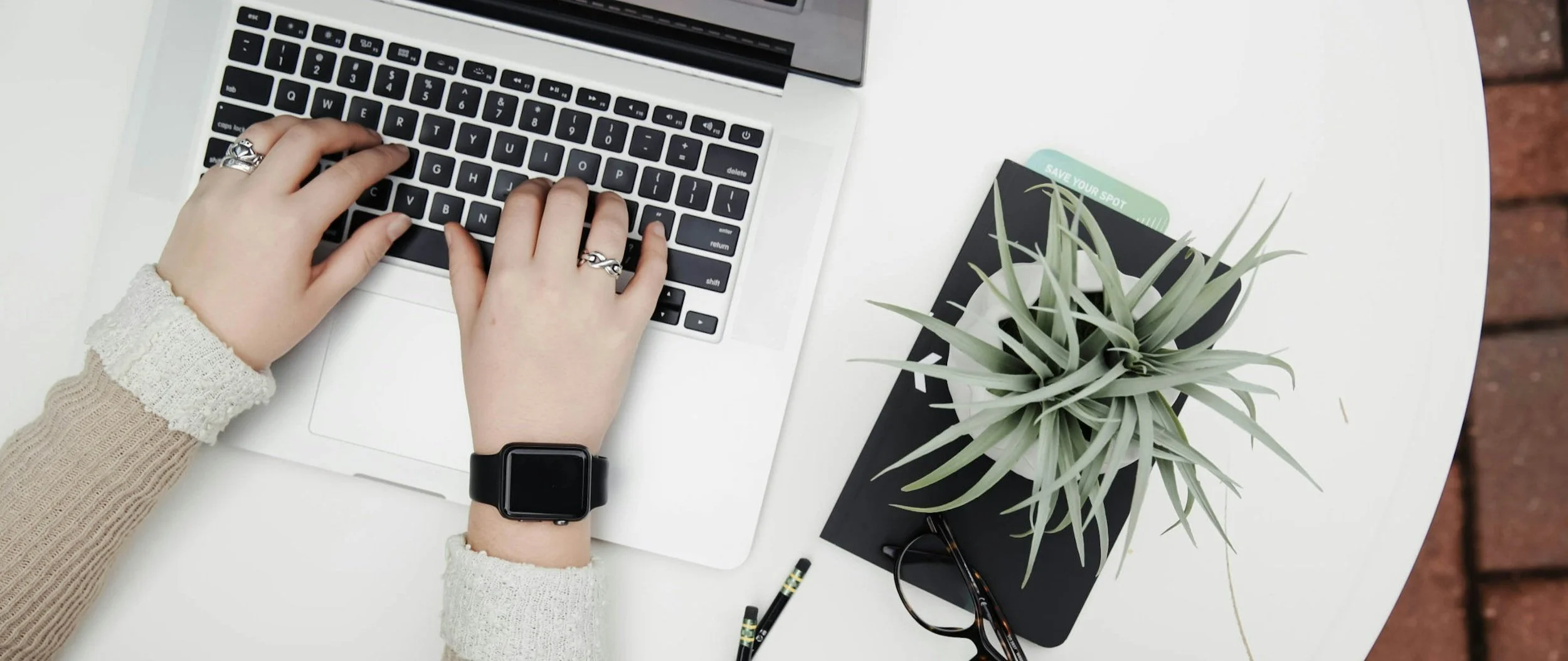 person typing on laptop minimalist photo wearing smart watch outdoors with plant