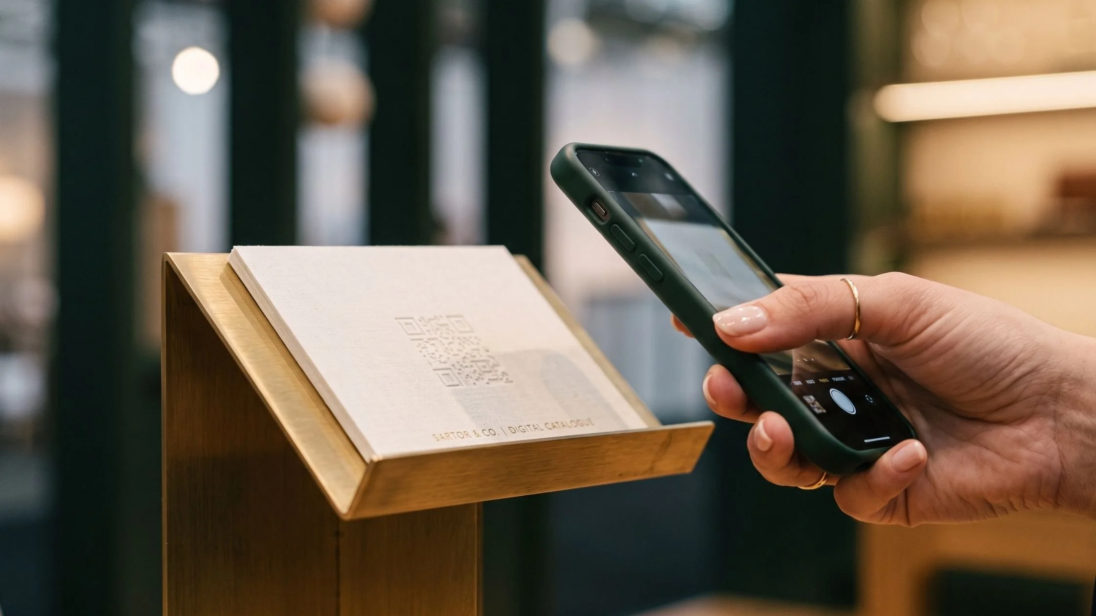 Close-up of a smartphone about to scan an architectural brass QR code display stand.