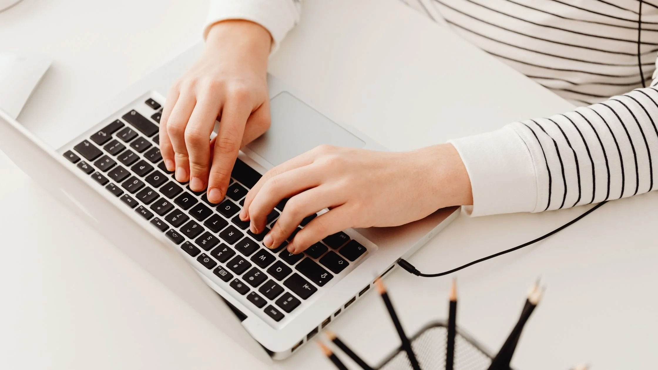 Overhead view of hands typing on a laptop on a clean, white minimalist desk.