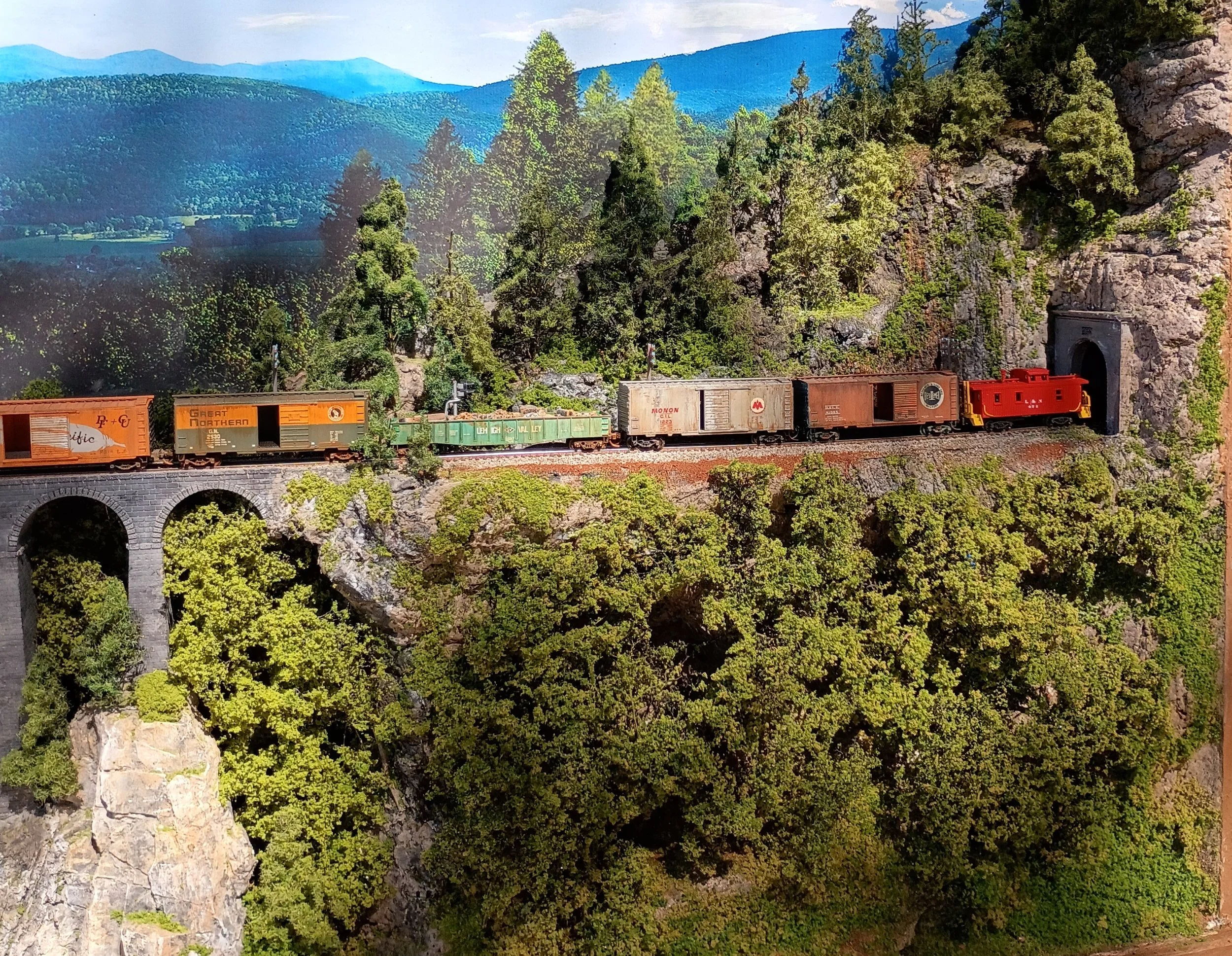 Model train moving through a detailed landscape with mountain background