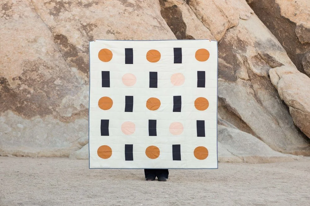 white cotton quilt with charcoal rectangles and orange and pink circles