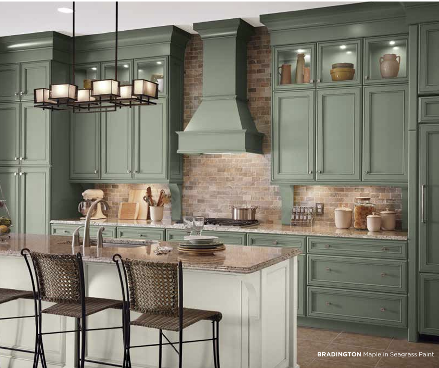 Modern kitchen with sage green cabinets, a brick backsplash, and a central island with seating. Includes hanging light fixture and various kitchen utensils and containers.