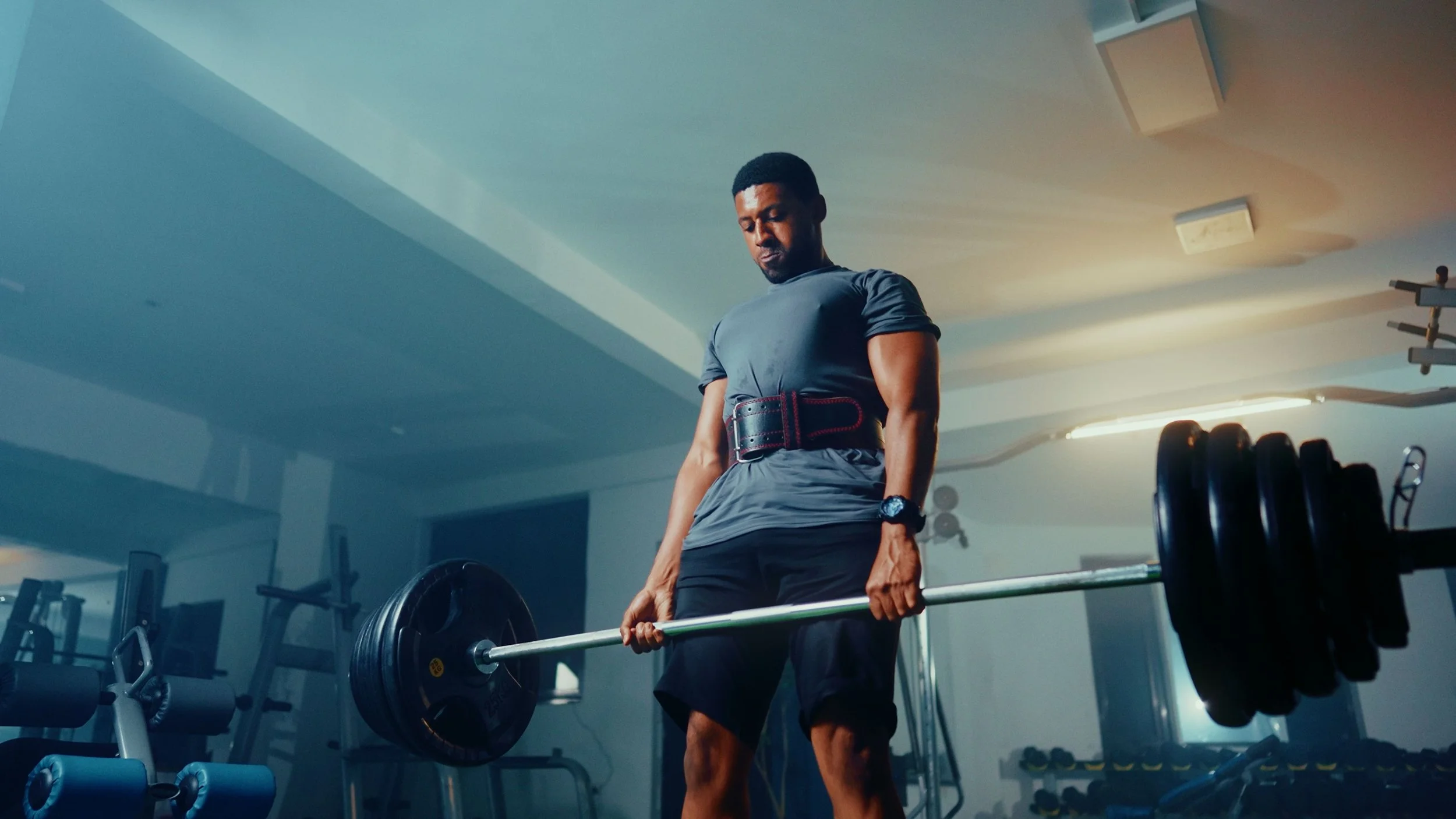 Man holding a loaded barbell at the top of a deadlift in a gym.