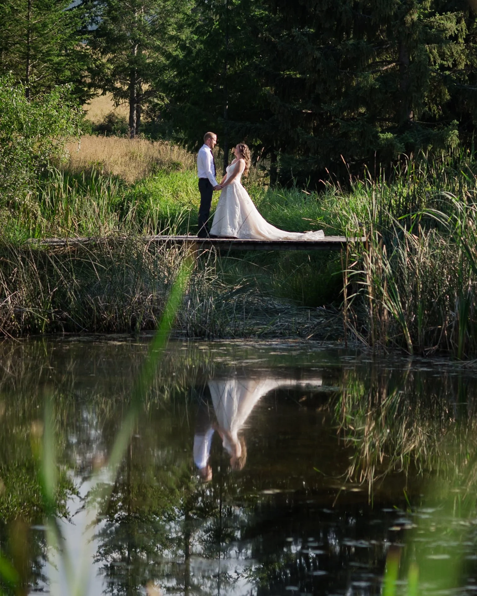 bride and groom walking across the pond on a bridge at rustic weddings