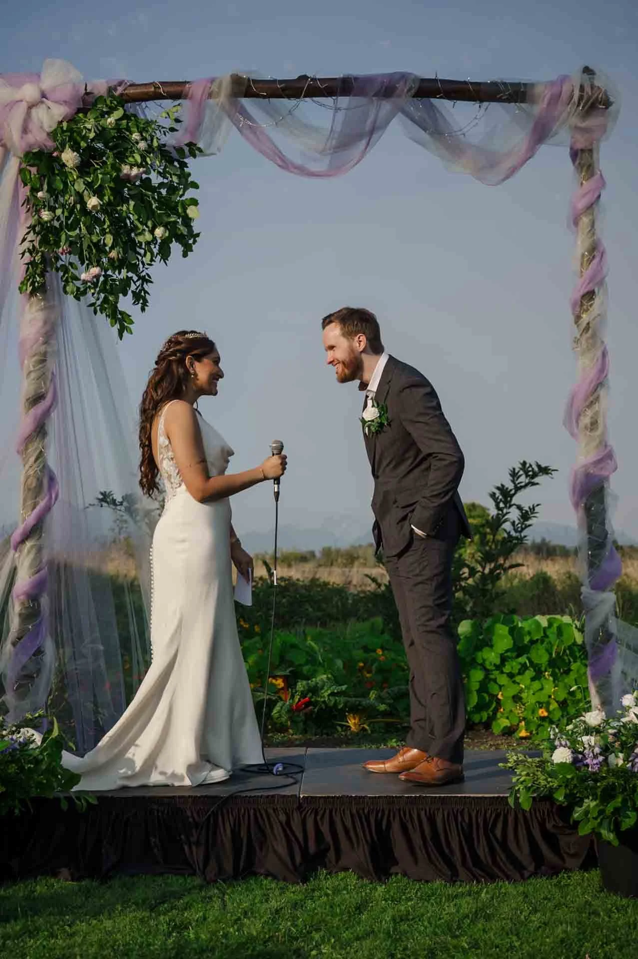 bride saying vows into a mic and groom laughing 