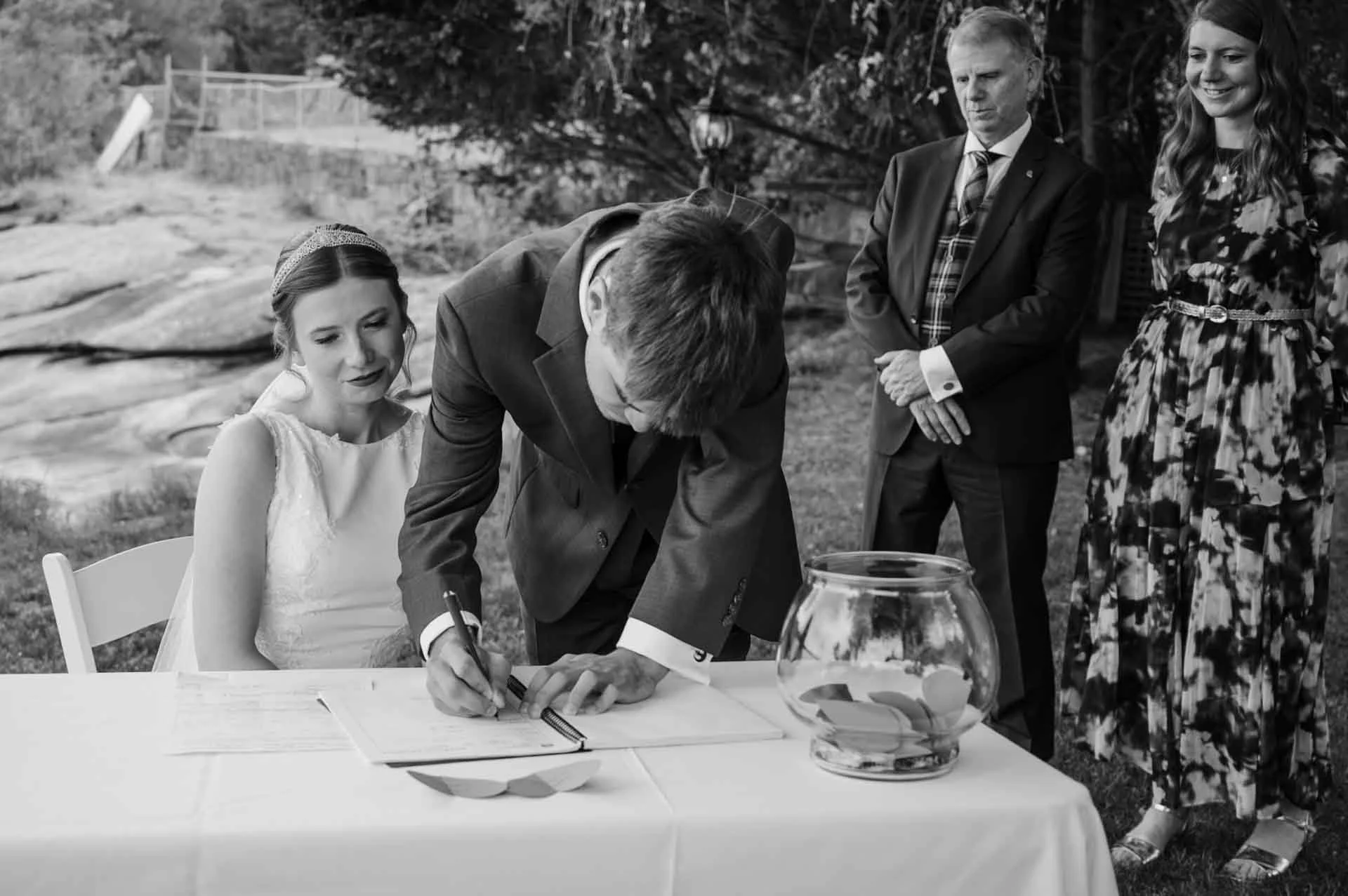 the groom signing the marriage license net to bride with witnesses standing in the background