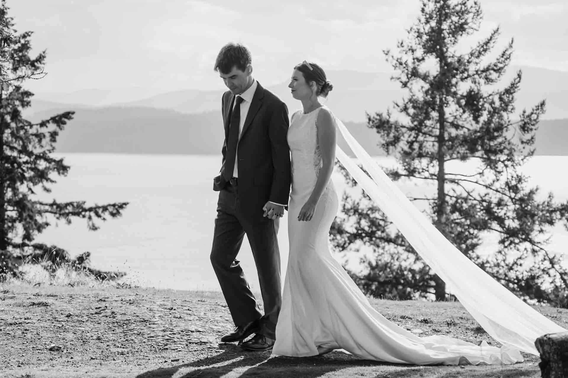 bride and groom walking with ocean and trees in the background