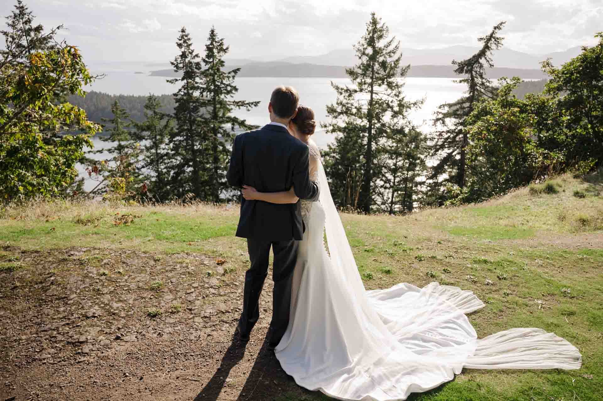 couple standing together in a side hug looking at a view of water, trees and grass