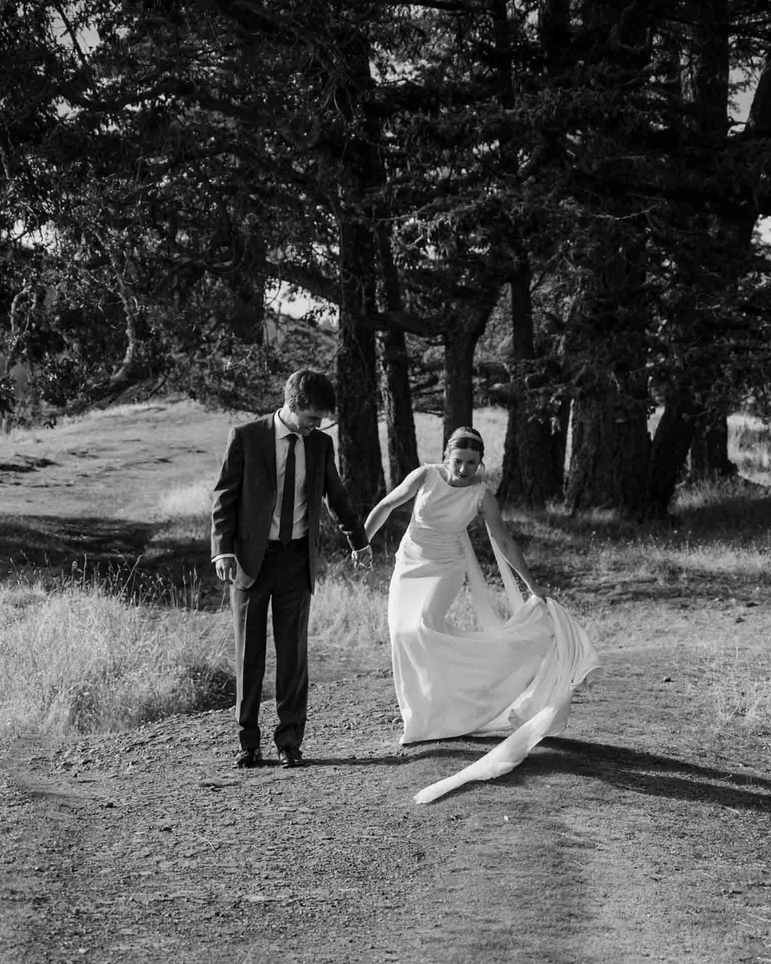 bride adjusting her wedding dress train as she holds the hand of her husband