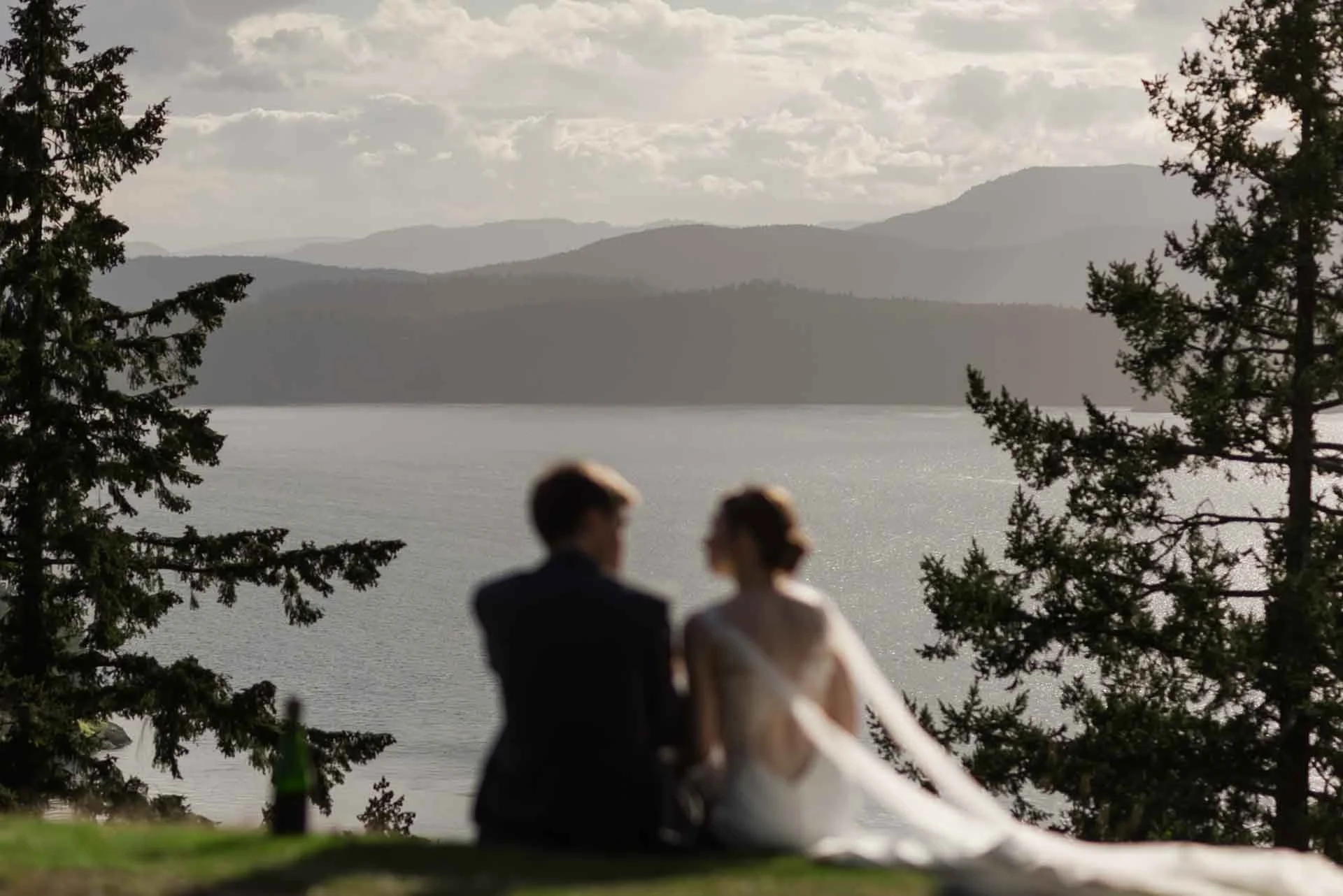 woman and man sitting looking at a view of water and mountains 