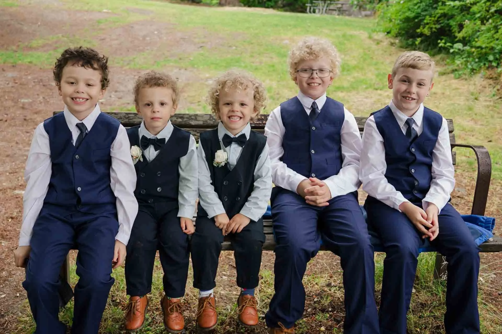 5 boys varying in age wearing matching suits on a bench