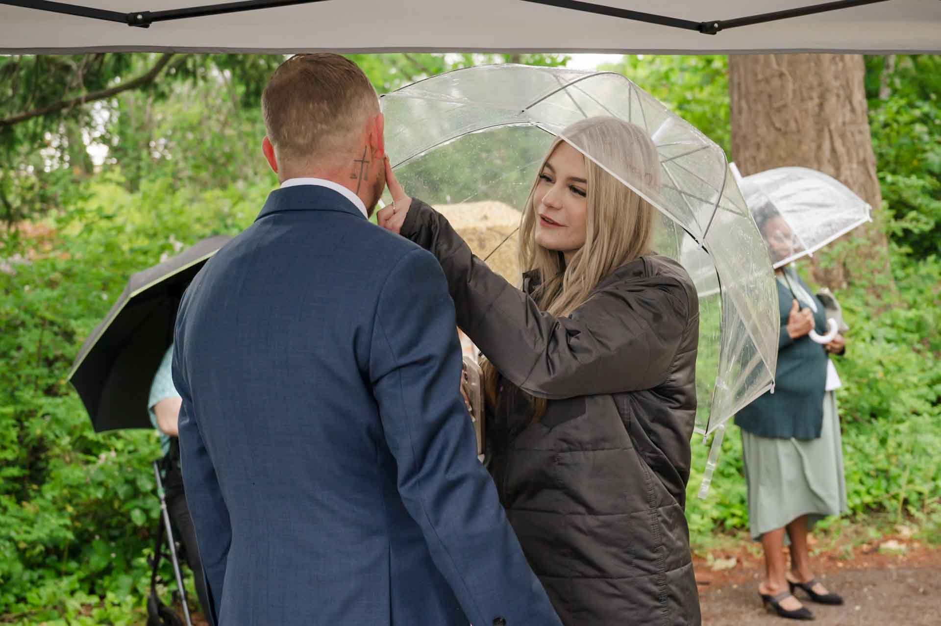 woman standing under an umbrella wiping the cheek of a man with her index finger