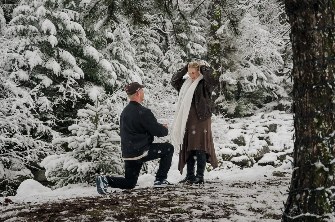 man down on one need in front of woman with snow covered trees in the background