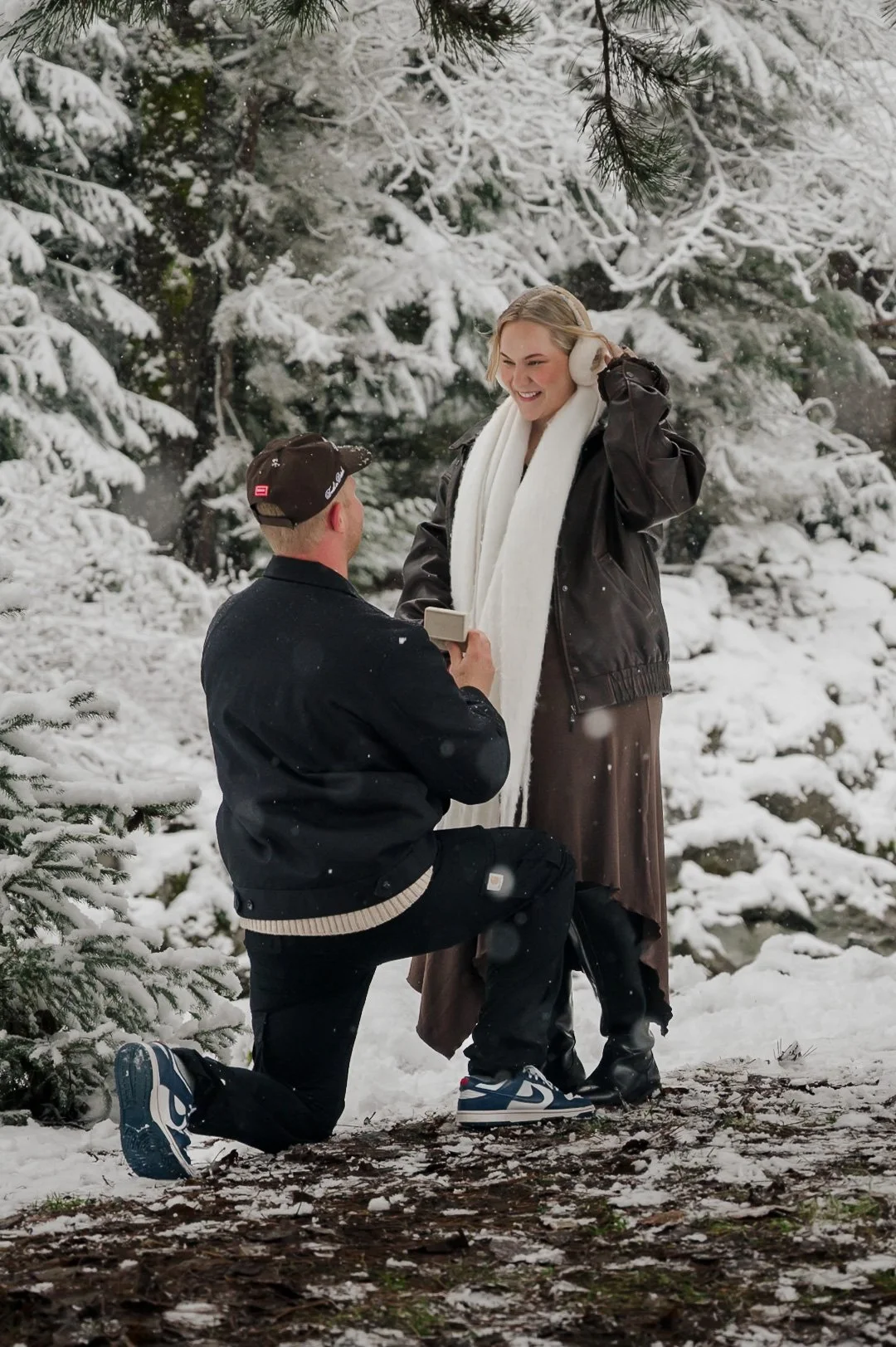 man proposing to woman in front of snow covered trees 