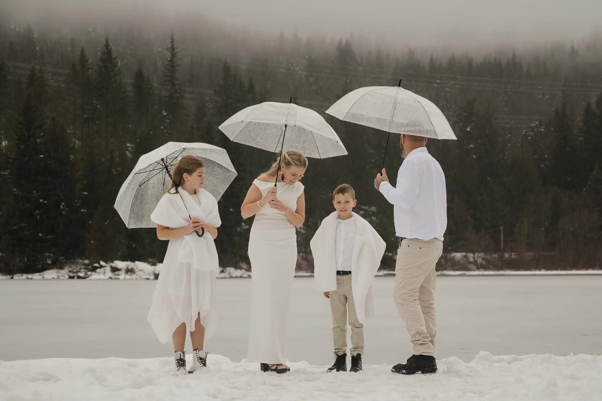 family standing on a snowy dock with a frozen lake and freeze in the background holding clear umbrella