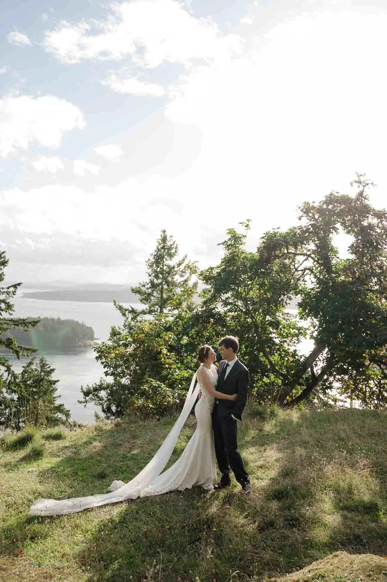 bride and groom facing each other, hugging, standing in a park overlooking the ocean