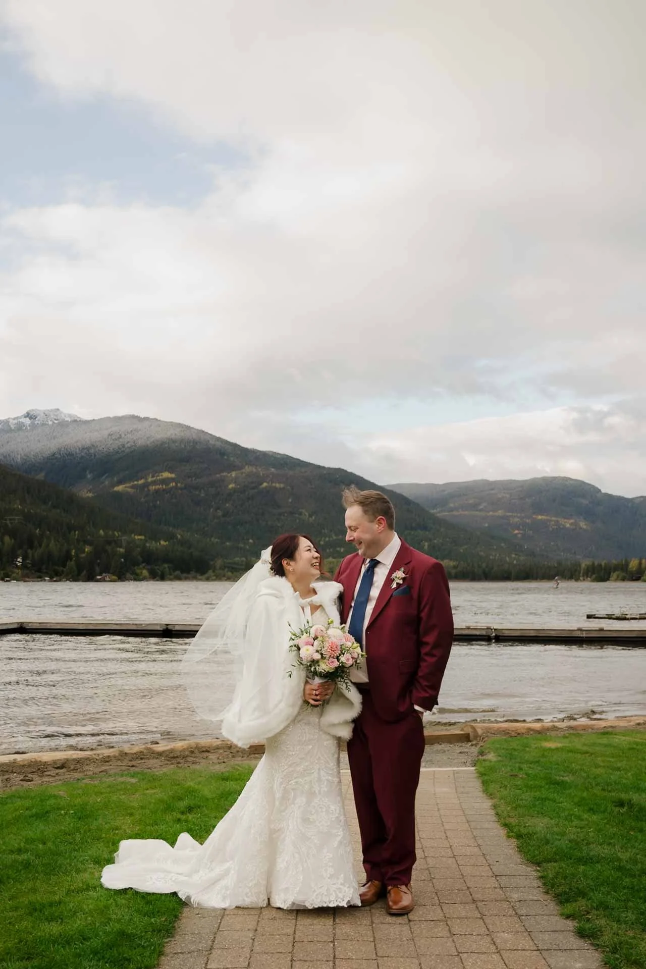 bride and groom in front of a lake with mountains in the background