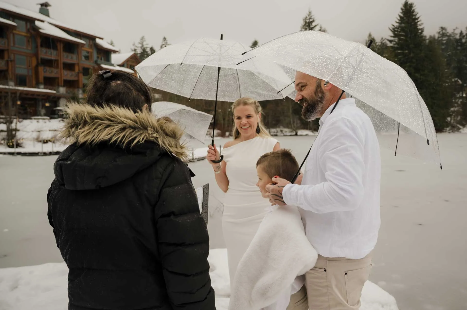 outdoor elopement ceremony in the rain, the couple with their kids, holding umbrellas on a dock on a frozen lake
