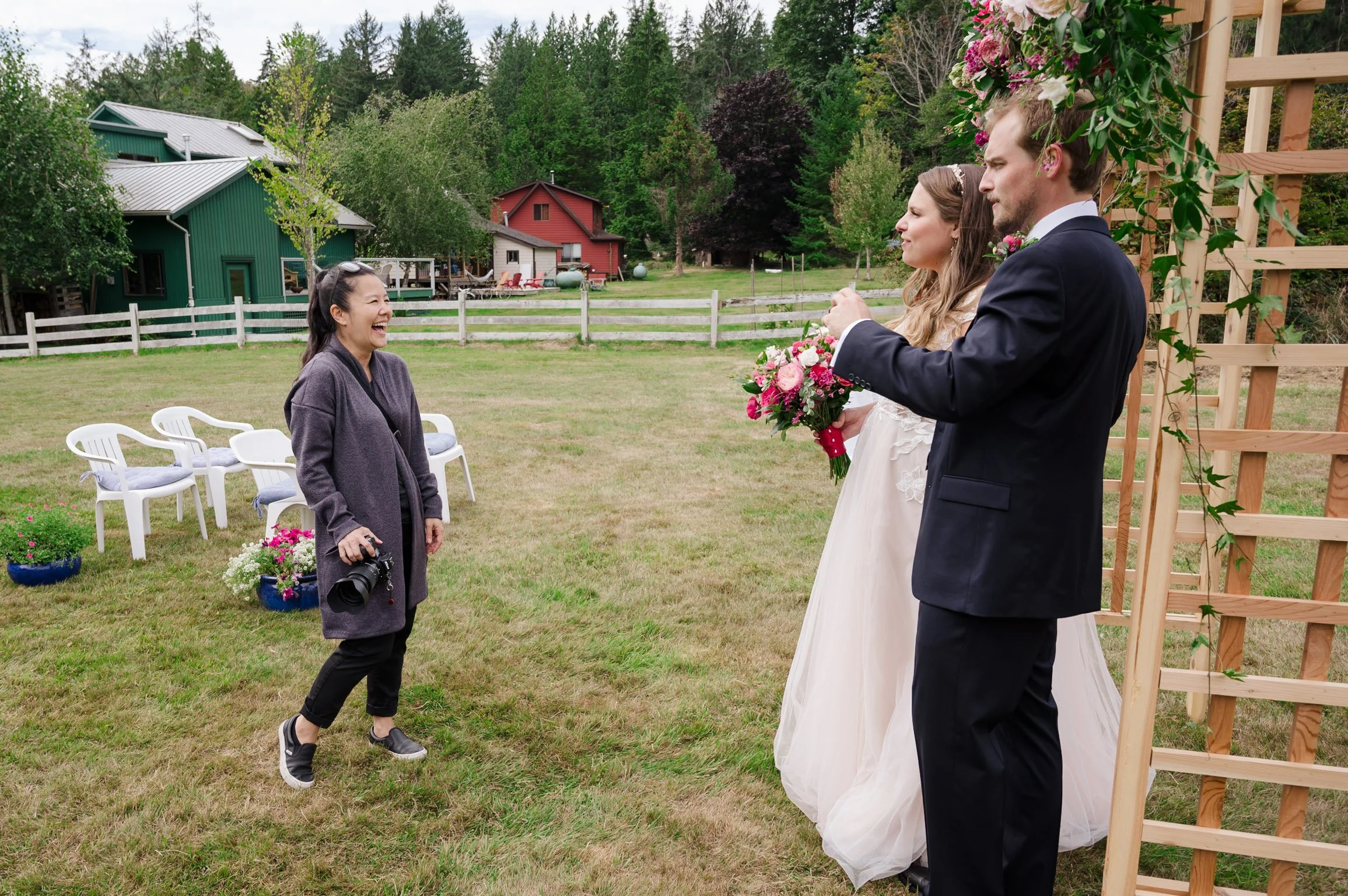 bride and groom standing next to an arch laughing with their wedding photographer.
